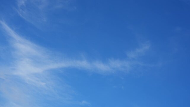 A blue sky timelapse captures delicate cirrus fibratus clouds stretching into feathery white streaks, shaped by high altitude winds and illuminated by soft sunlight in clear daytime weather. 4k.
