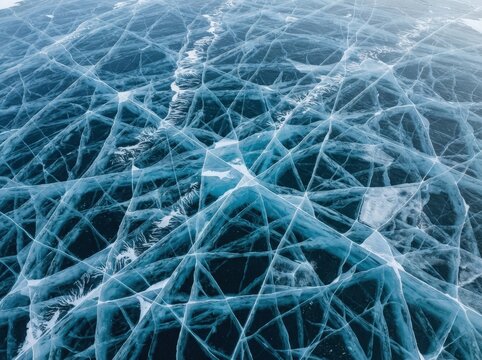 High angle view of clear blue frozen lake ice with intricate white crack patterns across the surface.