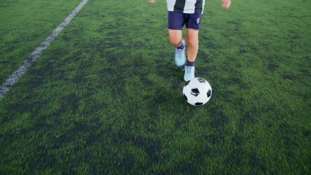 Close-up of a boy kicking a soccer ball on a green turf field, with sharp detail and frozen motion, representing youth sports, training, fitness and a healthy active lifestyle.