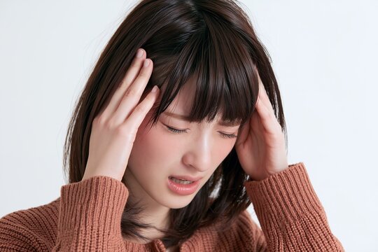 頭痛に苦しむ女性がこめかみを押さえる辛そうな表情