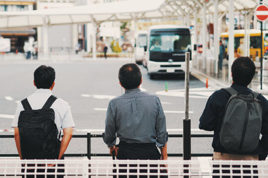 駅前のバス停で待つ人々の後ろ姿