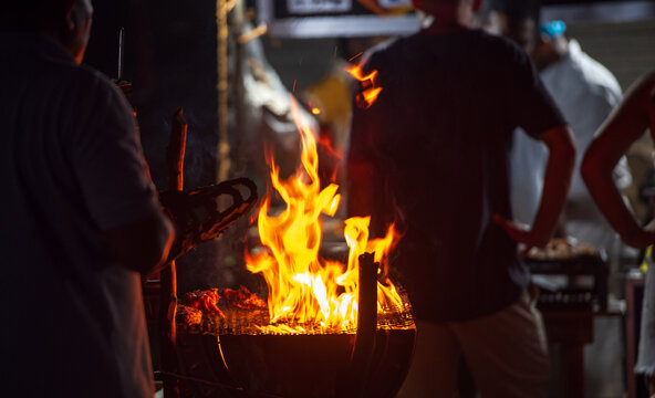 Street food barbecue grill with flames and vendors cooking at night
