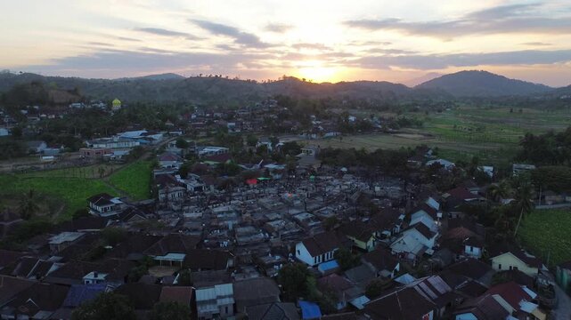 Aerial view of Sade Village with traditional thatched-roof houses and lush greenery at sunset in Pujut, West Nusa Tenggara, Indonesia.