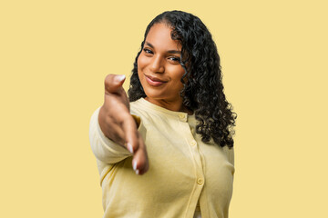 Woman, hispanic, curly hair, plus size, young, casual clothes, yellow sweater, offering handshake, business hand greeting shake, welcoming hands, success, friendly successful smiling, studio portrait © Krakenimages.com