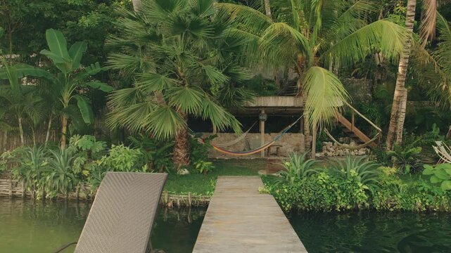 Idyllic nature retreat on Lake Peten Itza with a wooden dock, empty lounge chairs, lush tropical plants, and hammock, captured in soft natural daylight with peaceful reflections.