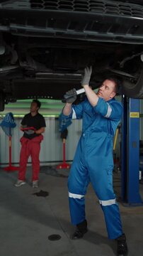 Mechanic inspects undercarriage with focused concentration. Second technician observes nearby with attentive posture