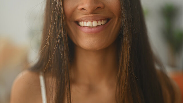 Woman smiling with visible teeth and long hair, bare shoulders and white strap in a studio interior portrait; happiness warmth.