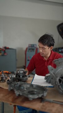 Focused technician inspects engine parts with care. Hands grip tools, notes, and mechanical components