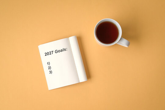 2027 goals and list on notepad next to cup of coffee on yellow background. Top view.
