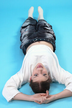 Playful Young Woman Lying Upside Down on Blue Background Sticking Out Tongue
