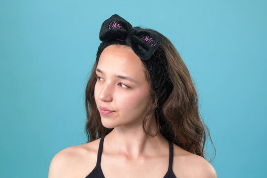 Young woman with black bow headband and OMG embroidery posing against a blue background