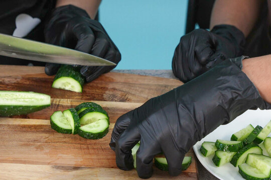 Chef in Black Gloves Slicing Cucumber on Wooden Cutting Board