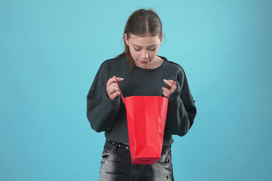 Curious Young Woman Looking Inside a Red Shopping Bag