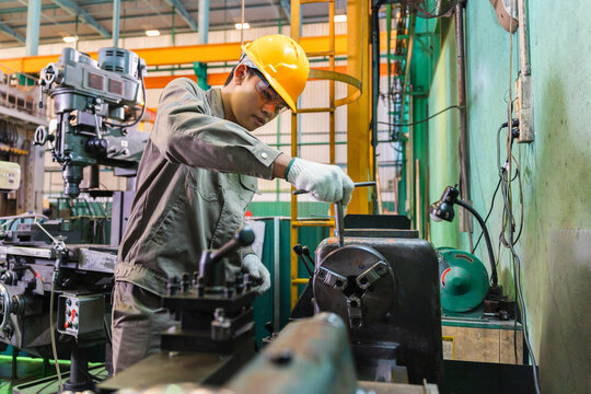 Asian male machinist operating metal lathe machine in industrial manufacturing factory, Industrial technician using T-wrench tool to adjust metal lathe chuck in workshop
