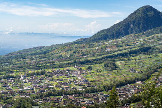Panoramic high angle view of rural village settlements and terraced agricultural fields on a mountain slope under blue sky