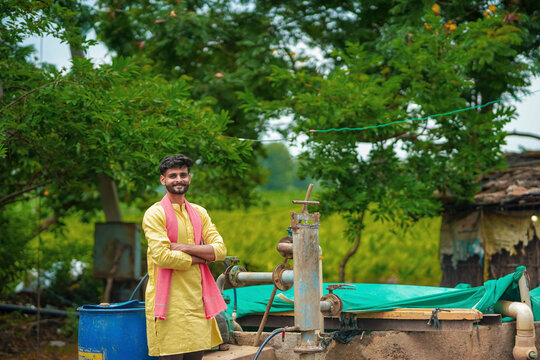young indian farmer standing with water hand pump at rural village