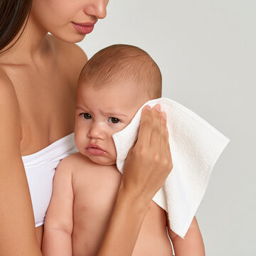 A mother tenderly wipes her baby's face with a soft cloth, conveying a moment of gentle care and maternal love