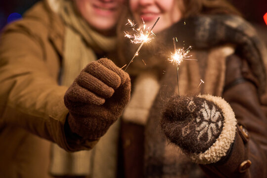 Caucasian young adult couple holding burning sparklers outdoors during winter holiday celebration. Closeup shot for festive season marketing and New Year advertising campaigns