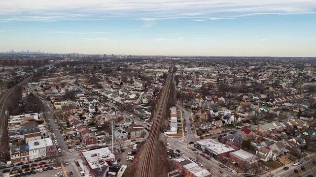 Drone glide along a railway corridor through low rise housing. Parallel railway tracks stretch toward the horizon between rows of houses with bare trees and pale rooftops under thin winter clouds.