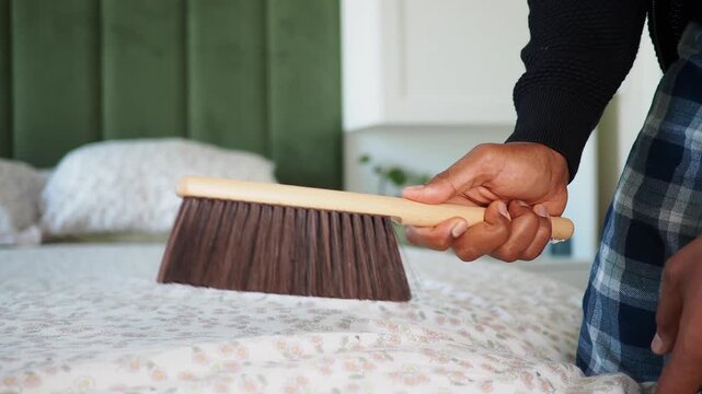 Person cleaning a bed with a dust brush in a bedroom setting