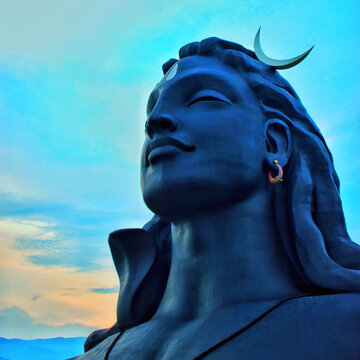 Low-angle close-up of the iconic dark blue Adiyogi Lord Shiva statue with a crescent moon against a vibrant blue sunset sky in Coimbatore, India.
