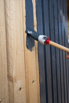 Streichen einer Holzoberfl&auml;che &ndash; links naturbelassen, rechts bereits dunkel gestrichen. Ein Pinsel tr&auml;gt frische Farbe auf die Holzplanken auf.