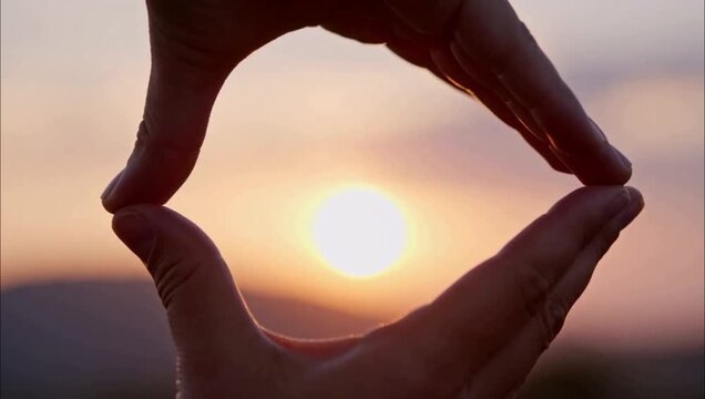 Close up of hands framing the bright sun during a beautiful golden sunset.