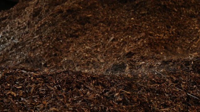 Close-up footage of a large pile of brown shredded wood chips and organic biomass material. The rough texture and layered fragments illustrate organic material processing, biomass resources, wood recy