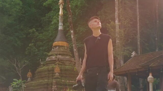 man traveler with camera at ancient Buddhist temple, Tourist visiting historic pagoda surrounded by forest at Thai cultural landmark Wat Phra Lat 4k