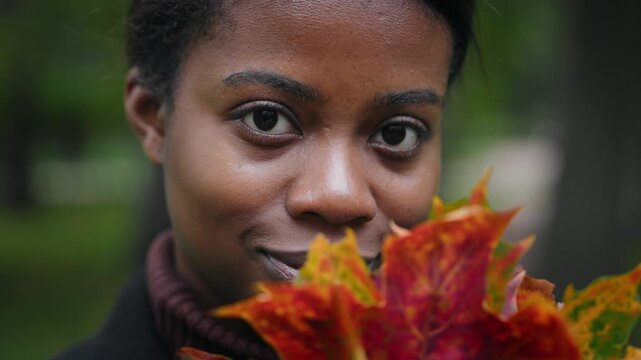 Female beauty and sensuality, closeup of african woman face in park in autumn. Charming lady looking at camera and smiling, fascinating big black eyes, natural clean face and nature, good mood