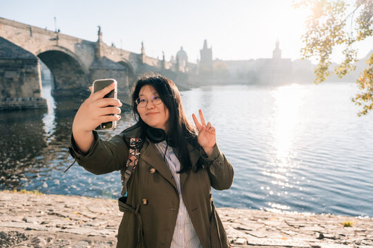 Asian female tourist takes selfie, river in Prague, sunny day