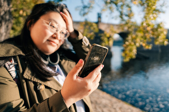 Person holding broken phone near river with bridge