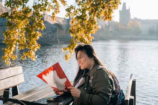 Korean tourist enjoys time by river in Prague looking at map