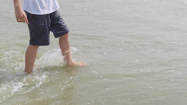 A boy is walking knee-deep in the sea slow motion and steps onto the sandy shore camera movement