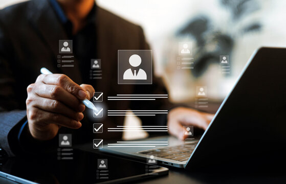 HR manager using a stylus to check boxes on candidate profiles on a digital screen near a laptop. Concept of human resources recruitment, candidate evaluation, and talent acquisition.