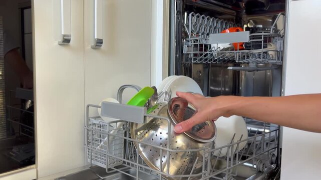 Close-up of woman unloading clean stainless steel colander and cutlery basket from a modern dishwasher