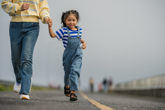 mother and preschool child girl holding hand and running on a road on mountain in morning