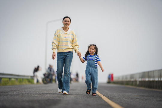mother and preschool child girl holding hand and walking on a road on mountain in morning