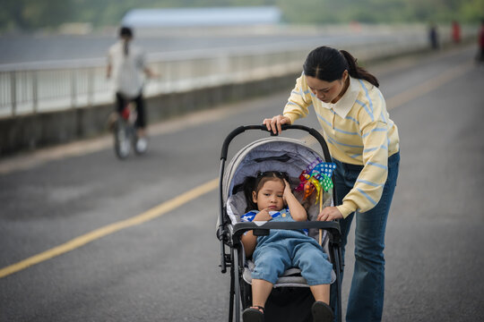 mother adjusting stroller shade for sleepy or headache little daughter outdoors on road