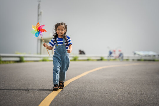 happy preschool child girl walking on road while holding a colorful pinwheel⁠