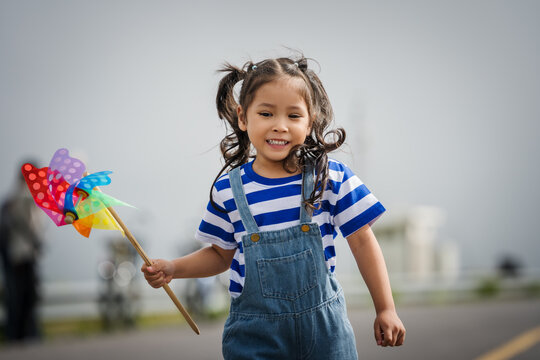 happy preschool child girl walking on road while holding a colorful pinwheel⁠