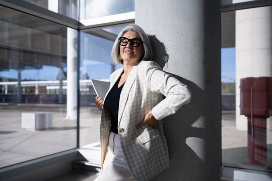 Businesswoman with laptop leans on a column inside modern building