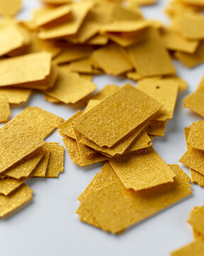 Golden confetti sparkles softly against a clean white background. Each piece has a textured, glittery surface that catches light. Delicate, rectangular shapes create a festive, celebratory feel