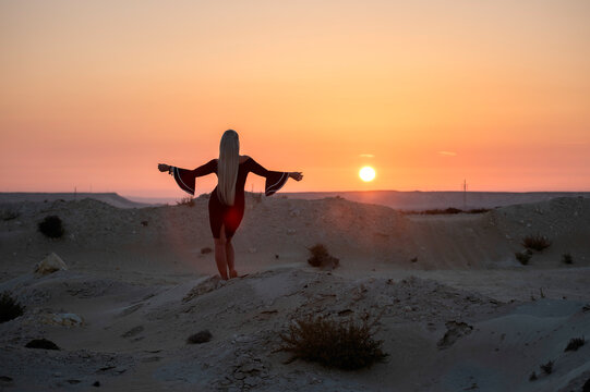Zikreet, Qatar - April 10, 2026: Silhouette of a woman standing on desert sand dunes with arms outstretched toward a golden sunset. a woman enjoying freedom and serenity during golden hour in a rocky 