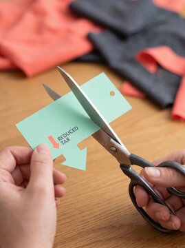 tax planning deduction paperwork profit concept. Person cutting a paper arrow labeled "Reduced Tax" with scissors