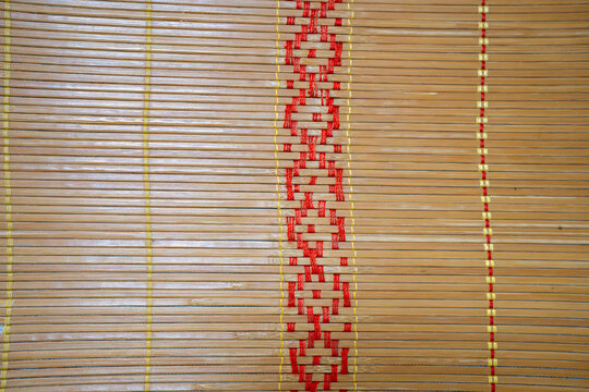 Close-up of intricately woven bamboo mat featuring vibrant red and yellow designs.