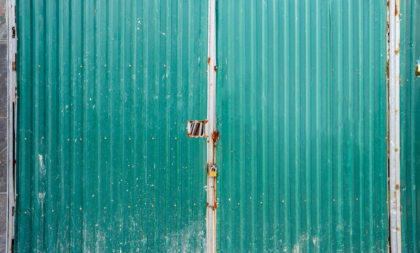 Textured green corrugated metal doors with rust and a padlock.