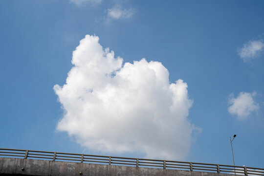 A fluffy white cloud floating in a clear blue sky above a concrete overpass.