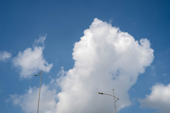 Fluffy white clouds against a bright blue sky, with streetlights in the foreground.