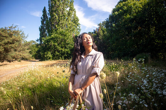 Woman stands in a sunny green field enjoying nature and flowers